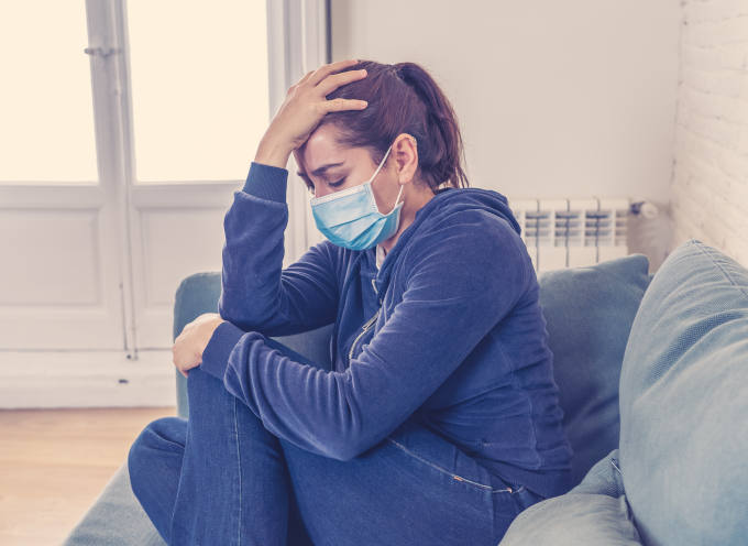 Sad woman with protective face mask at home