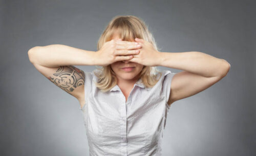 Young woman portraits on grey background, covering her eyes